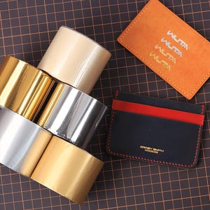 May include: A selection of craft materials featuring rolls of gold, silver, and beige metallic tape, and two leather cardholders. One is orange with "WUTA" text, the other is black with red accents and "CRAZY SMITH HANDMADE" text.