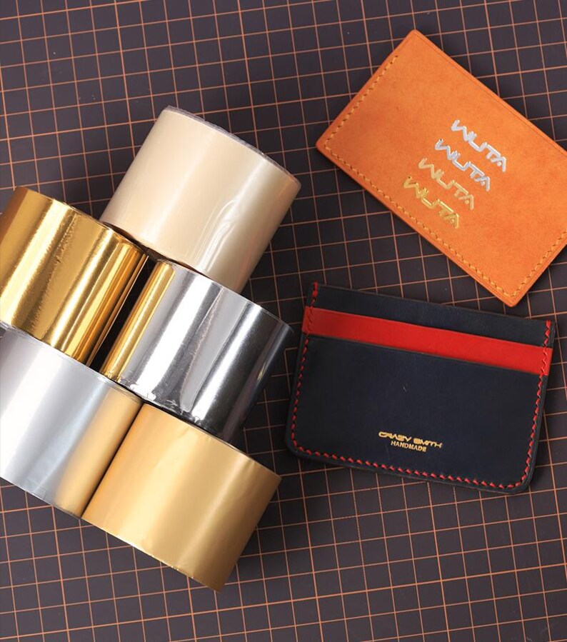 May include: A selection of craft materials featuring rolls of gold, silver, and beige metallic tape, and two leather cardholders. One is orange with "WUTA" text, the other is black with red accents and "CRAZY SMITH HANDMADE" text.