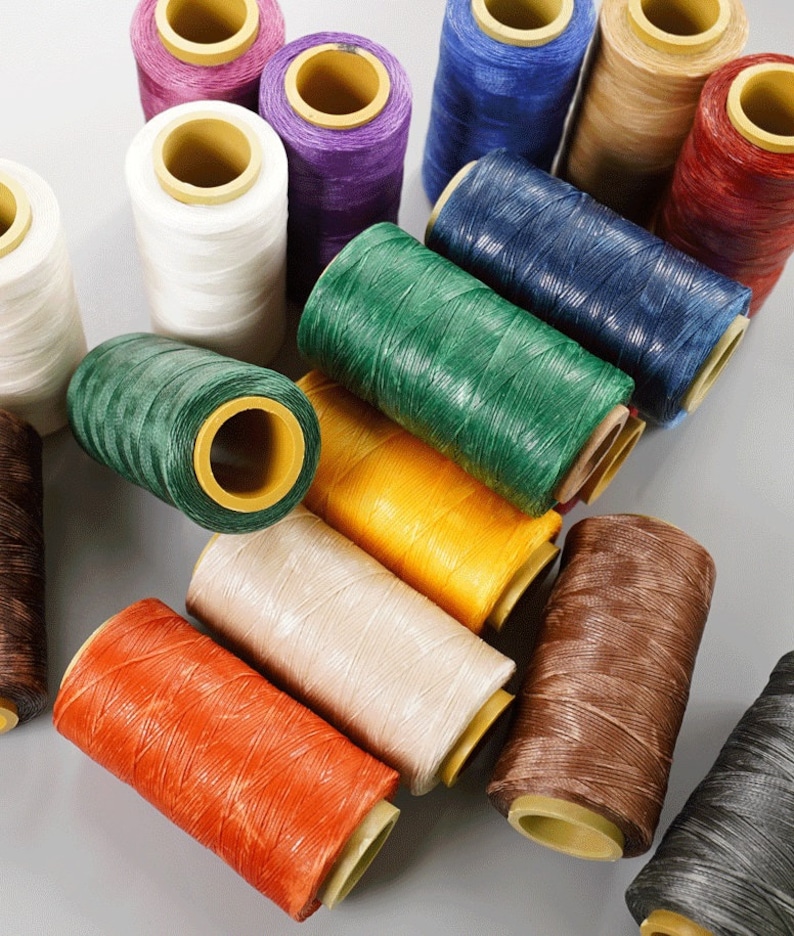 May include: A collection of spools of colorful thread in various shades, including white, purple, green, yellow, orange, beige, brown, and blue. The thread is tightly wound around cardboard cores, ideal for crafting and sewing projects.