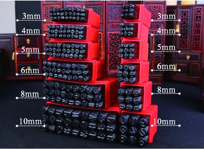 Puede incluir: Un conjunto de sellos de metal negro con letras y n&uacute;meros en cajas de almacenamiento rojas. Los tama&ntilde;os var&iacute;an de 3 mm a 10 mm. Los sellos est&aacute;n dispuestos en una exhibici&oacute;n apilada, mostrando varias fuentes y tama&ntilde;os.