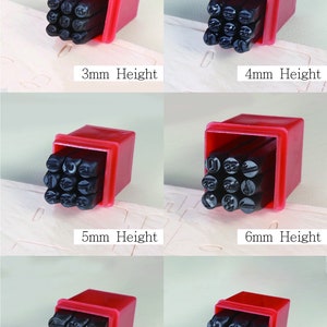 Puede incluir: Un juego de sellos num&eacute;ricos en una caja de pl&aacute;stico roja. Los sellos son negros y vienen en varias alturas: 3 mm, 4 mm, 5 mm, 6 mm, 8 mm y 10 mm. El texto "Set of numbers" est&aacute; en la parte superior de la imagen.