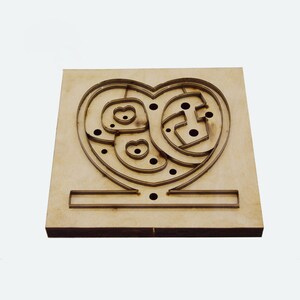 May include: A wooden heart-shaped puzzle with a series of pathways and circular cutouts. The puzzle is made of light brown wood and has a rectangular base. The design is cut out of the wood.