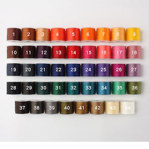 May include: A collection of 44 spools of colorful thread, each labeled with a number from 1 to 44. The threads span a wide spectrum of colors, including shades of brown, orange, red, pink, purple, blue, green, and yellow. Ideal for crafting and sewing projects.