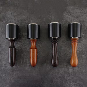 Puede incluir: Cuatro tapones de botella con tapas negras y detalles plateados. Los mangos de madera varían en color, desde marrón oscuro hasta marrón claro. Dispuestos sobre un fondo gris oscuro.