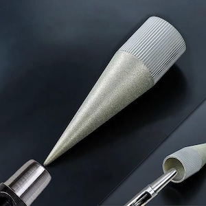 Puede incluir: Una herramienta de esmerilado cónica de color plateado con un mango texturizado y estriado. La herramienta se estrecha hasta un punto afilado y está diseñada para trabajos de precisión. La imagen muestra la punta de la herramienta alineada.