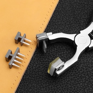 May include: A leathercraft tool set featuring a silver metal stitching punch and two metal punches with multiple prongs. The tools are next to a piece of tan leather with pre-punched stitch holes. The background is black.