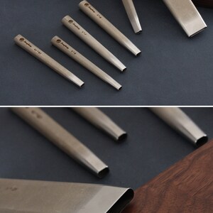 May include: A collection of silver metal leather working tools, including punches of different sizes and a rectangular tool. Each tool is marked with a size and a logo. The tools are arranged on a dark surface and a wooden cutting board.
