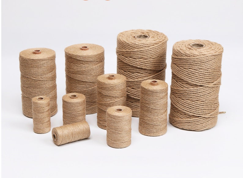 May include: A collection of various-sized spools of natural-colored twine. The twine is tightly wound around a central core, with a visible wooden center. The spools are arranged on a white surface, showcasing the different sizes available.