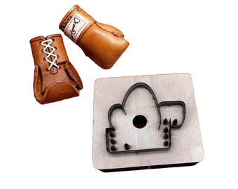 Peut inclure: Deux mini gants de boxe en cuir marron et une matrice métallique d'un gant de boxe. L'un des gants a des lacets blancs et l'autre porte une étiquette avec l'inscription "Champion". La matrice est sur un bloc de bois.