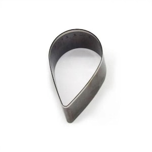 Könnte beinhalten: Eine tropfenförmige Metall-Lederstanzform. Die Form ist dunkelgrau und hat eine abgerundete Oberseite und eine spitz zulaufende Unterseite. Der Innenraum ist hohl und weiß. Für Lederarbeiten.