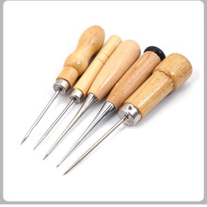 May include: A collection of five awls with wooden handles. The awls have polished metal tips and vary in handle shape and wood grain. The handles are light brown and tan, and the metal tips are silver.