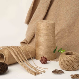 May include: An assortment of natural jute twine and rope in various forms. The image shows a large spool, a smaller roll, and a ball of twine, along with decorative woven spheres and burlap fabric in the background.