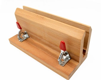May include: A wooden woodworking clamp with a natural finish. The clamp features two red toggle clamps and a channel for holding materials. The wood has a light brown color and a smooth texture. The clamp is designed for woodworking projects.