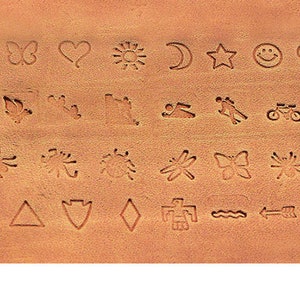 May include: A close-up of a tan leather surface featuring embossed designs. These include a leaf, butterfly, heart, sun, moon, star, smiley face, flower, and other nature-inspired and geometric shapes. The surface has a textured appearance.