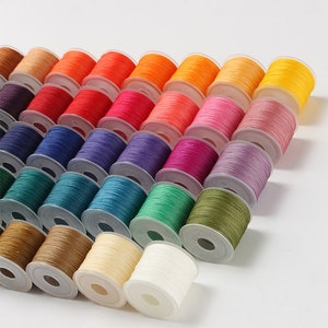May include: A collection of colorful spools of thread arranged diagonally. The spools display a wide spectrum of colors, including shades of orange, red, pink, blue, green, and yellow. The thread is neatly wound on white plastic spools, ideal for sewing and crafting projects.