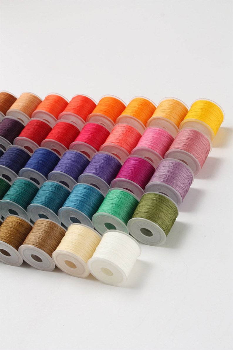May include: A collection of colorful spools of thread arranged diagonally. The spools display a wide spectrum of colors, including shades of orange, red, pink, blue, green, and yellow. The thread is neatly wound on white plastic spools, ideal for sewing and crafting projects.