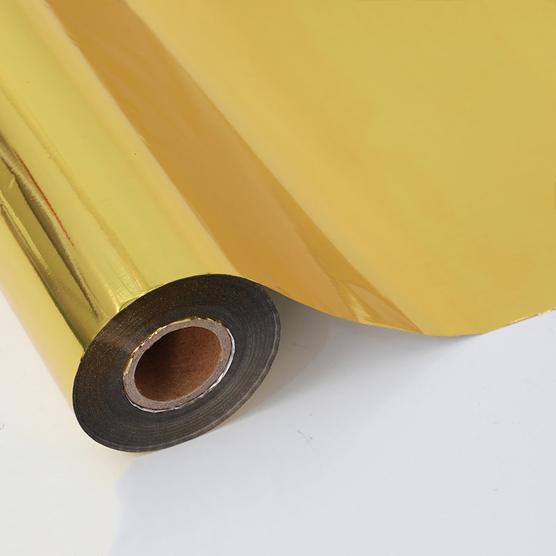 May include: A roll of shiny gold foil paper. The foil is tightly wound around a cardboard core, with a portion unrolled, revealing its reflective surface. The gold colour is consistent throughout the roll, creating a bright, metallic appearance.