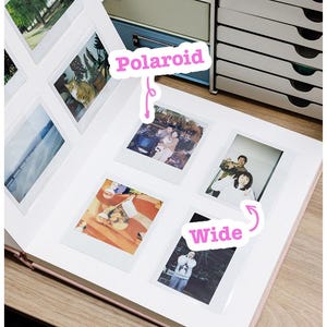 Op de afbeelding: Een roze fotoalbum met verschillende Polaroid-foto's. Het woord "Polaroid" staat op een roze sticker. Het woord "Wide" staat op een roze sticker. Het album is open op een houten oppervlak.