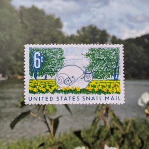 May include: A rectangular postage stamp featuring a white snail with a small mail bag, set against a background of green trees and yellow flowers. The stamp displays the number 6c and the text UNITED STATES SNAIL MAIL in blue lettering.