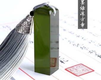 May include: A green rectangular stamp with a silver tassel. The stamp is on a white surface with red lines. The text "墨 俠 方 章" is written in black on a white background.