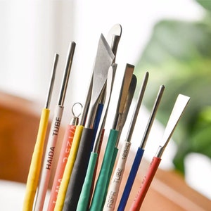 May include: A set of ten metal sculpting tools with various shapes and sizes. The tools are arranged in a fan shape and have colorful heat shrink tubing on the handles. The tubing is labeled with the text "HAIDA TUBE" and "RSFR TUBE 125C".