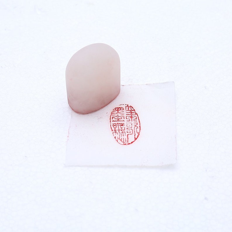 May include: A white oval-shaped stamp with a red ink impression of Chinese characters. The stamp is on a white surface.