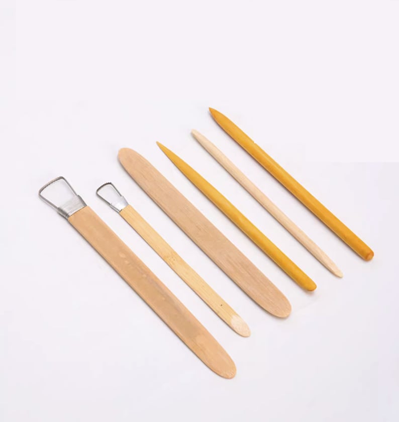 May include: A set of six wooden sculpting tools, including a loop tool, a scraper, and four different sized modeling tools. The tools are made of natural wood and have a light brown color.