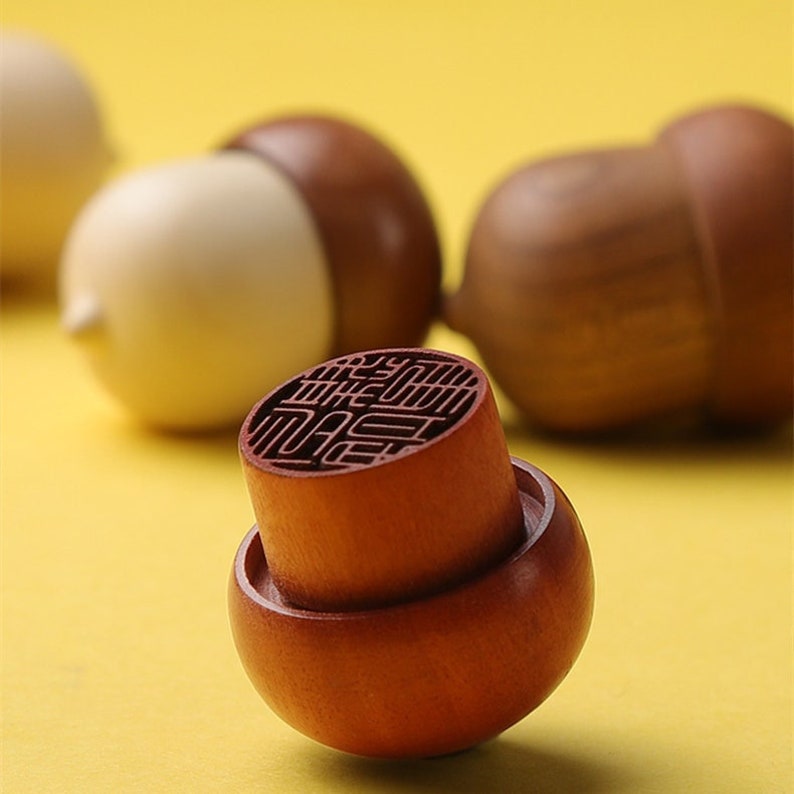 May include: A wooden acorn-shaped stamp with a circular design on the top. The stamp is brown and has a light brown base. The design on the top is a traditional Chinese character.