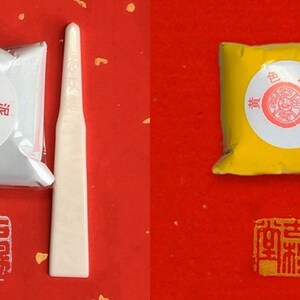 May include: Two small packets of powdered paint, one silver and one yellow, with a white plastic spatula next to each. The packets have Japanese text on them that reads "色 印泥".