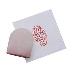 May include: A white, rounded, ink pad with a red imprint of a Chinese character on a white paper background.