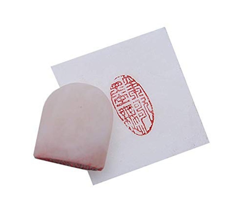 May include: A white, rounded, ink pad with a red imprint of a Chinese character on a white paper background.