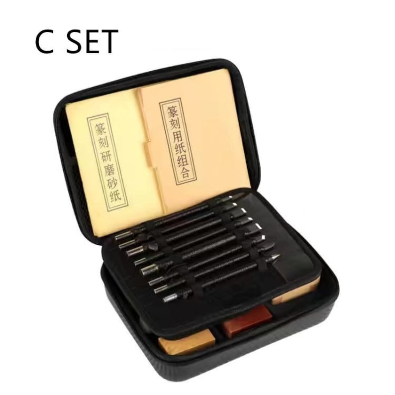 May include: A black carrying case with a zippered opening, containing a set of tools for carving. The case is open and the tools are visible. The tools are arranged in a row and are made of metal. The case also contains two small books with Chinese characters.
