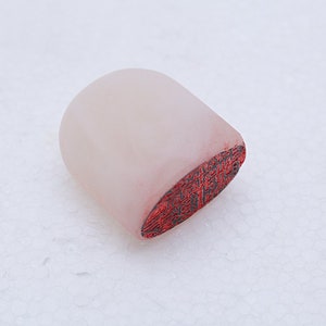 May include: A white, oval-shaped, carved stone seal with a red, detailed design on the bottom.