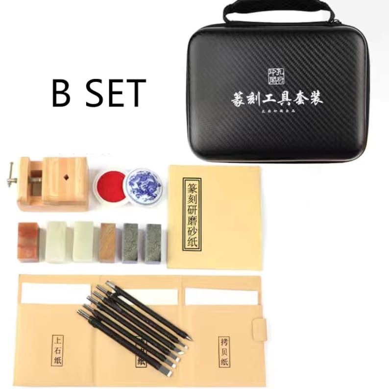 May include: A black carrying case with the text "篆刻工具套装" in white. The case contains a set of tools for carving seals, including a wooden handle with a metal blade, a red ink pad, a small ceramic dish, and a variety of carving tools. The set also includes a book with the text "篆刻研修体系" in black.