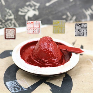 May include: A red ink pad with a small amount of ink in it. There are three small square stamps with Chinese characters on them. The stamps are in red, yellow, and black.