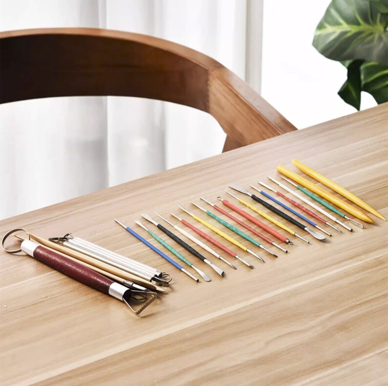 May include: A set of 20 clay sculpting tools with various shapes and sizes. The tools have colorful handles and are arranged on a wooden surface.