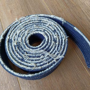 Pu&ograve; includere: Una cintura blu di arti marziali con bordi sfilacciati &egrave; arrotolata e annodata.
