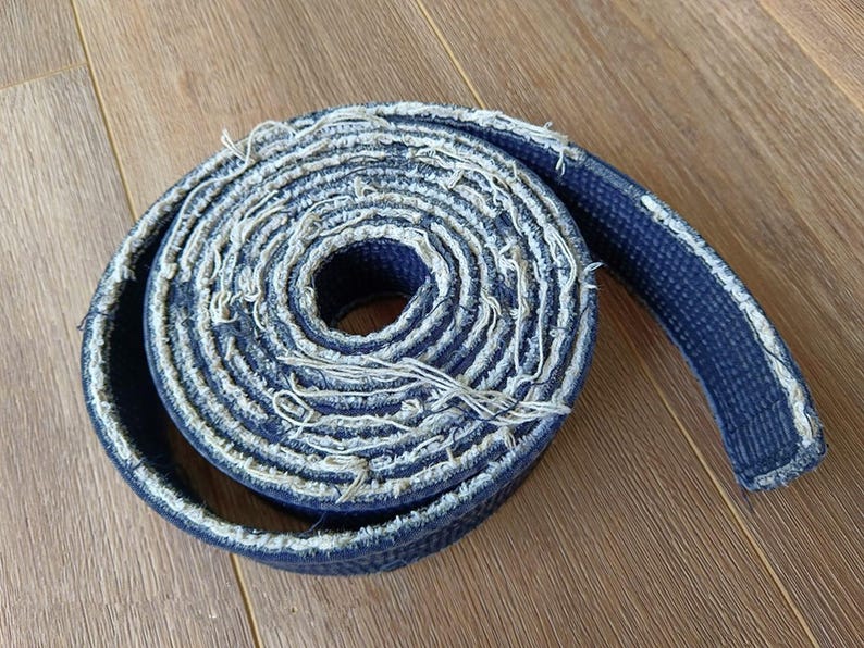 Pu&ograve; includere: Una cintura blu di arti marziali con bordi sfilacciati &egrave; arrotolata e annodata.