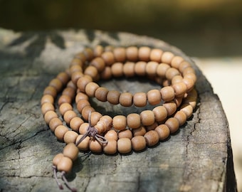 May include: A brown wooden mala bead necklace with a brown cord. The beads are round and smooth, and the cord is tied with a knot at the end.