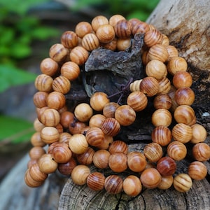 May include: A wooden beaded necklace with brown and light brown beads. The beads are round and have a striated pattern. The necklace is lying on a piece of wood.