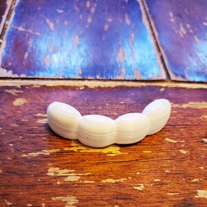 May include: A white plastic 3D printed object shaped like a row of four connected beans.