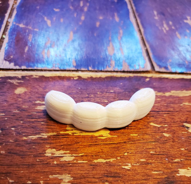 May include: A white plastic 3D printed object shaped like a row of four connected beans.