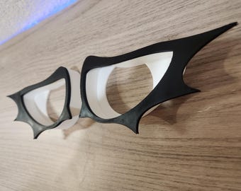 Könnte beinhalten: Zwei schwarze und weiße augenförmige Schablonen mit einem gezackten Rand. Die Schablonen sind aus flexiblem Material gefertigt und für Bastelarbeiten oder Dekorationen gedacht.