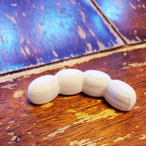 May include: A white, 3D printed, segmented, curved shape resembling a caterpillar or a worm.