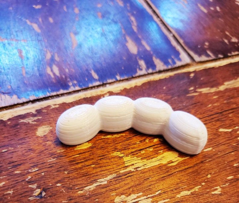 May include: A white, 3D printed, segmented, curved shape resembling a caterpillar or a worm.