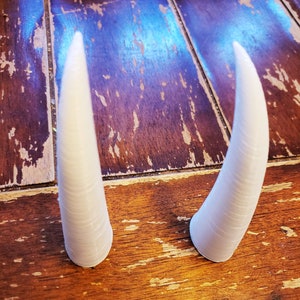 May include: Two white, plastic, pointed horns on a wooden surface.