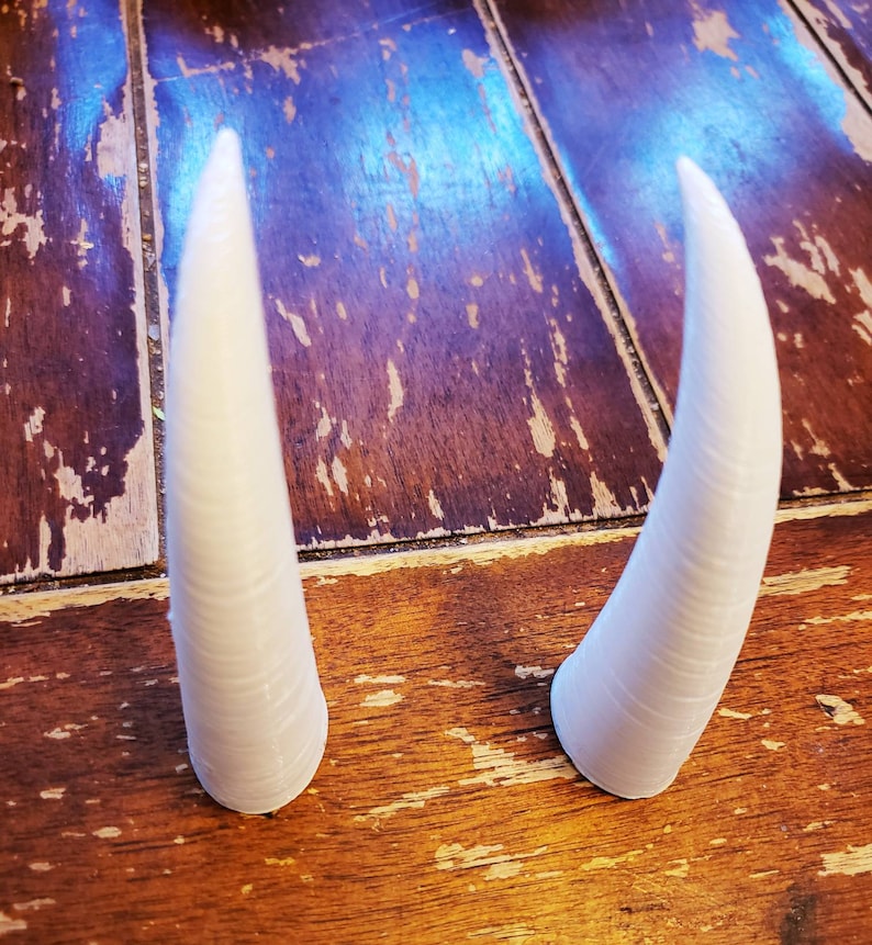 May include: Two white, plastic, pointed horns on a wooden surface.