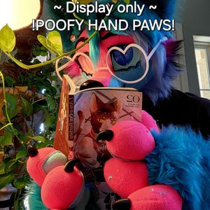 May include: A furry blue and pink character with large, pink, fluffy hands. The character is wearing heart-shaped glasses and holding a book titled "I Am a Cat Boyuta".