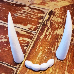 May include: Two white, 3D printed, pointed horns and a row of five white, 3D printed, rounded teeth.