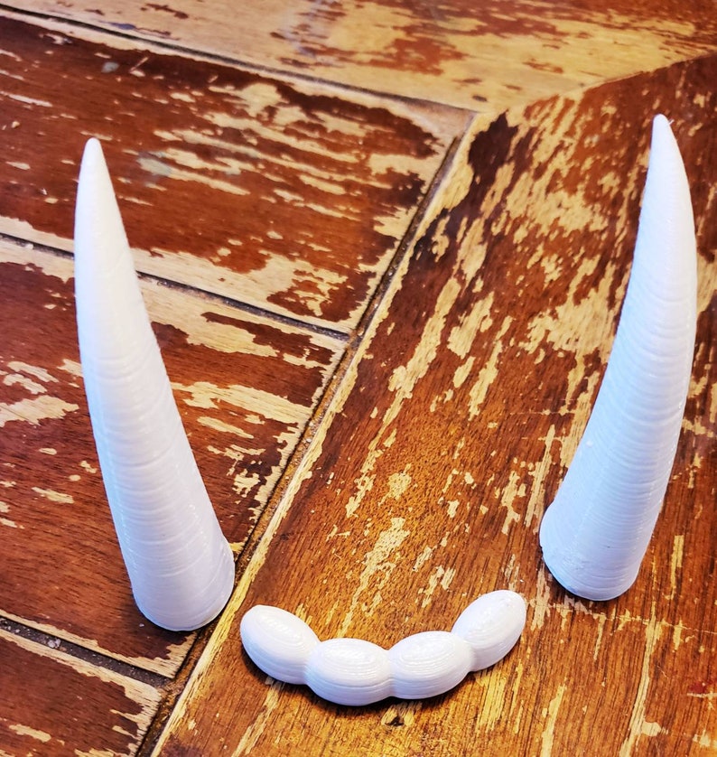 May include: Two white, 3D printed, pointed horns and a row of five white, 3D printed, rounded teeth.